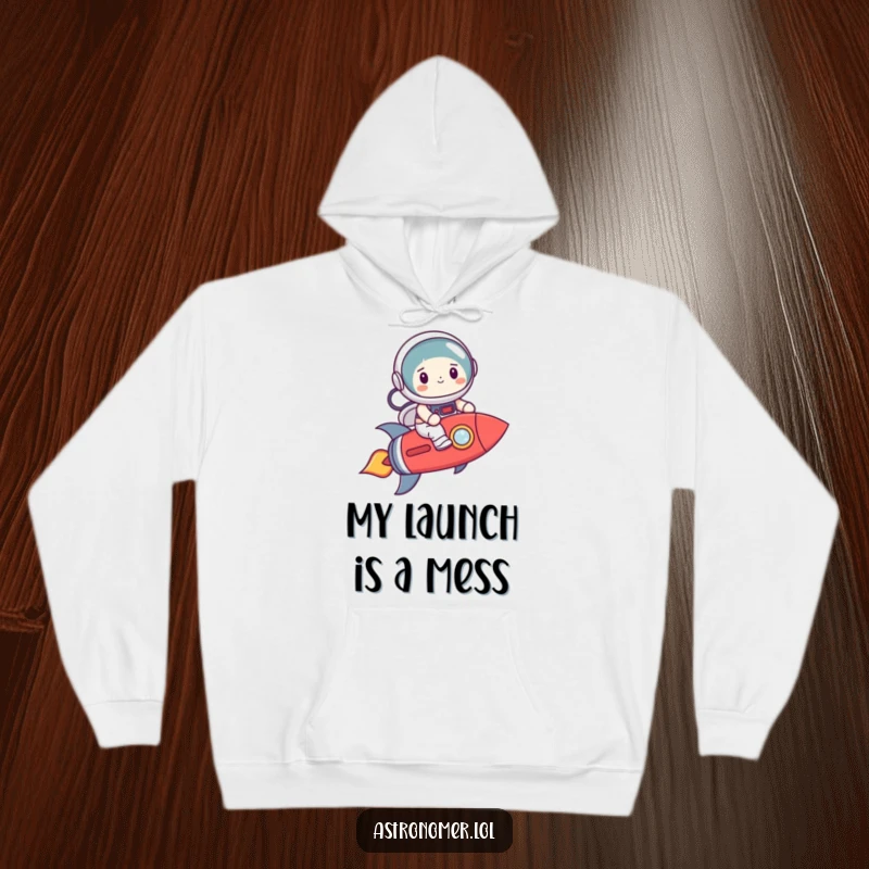 Funny astronaut character smiling nervously while riding a crooked rocket, cozy and humorous hoodie for space enthusiasts.