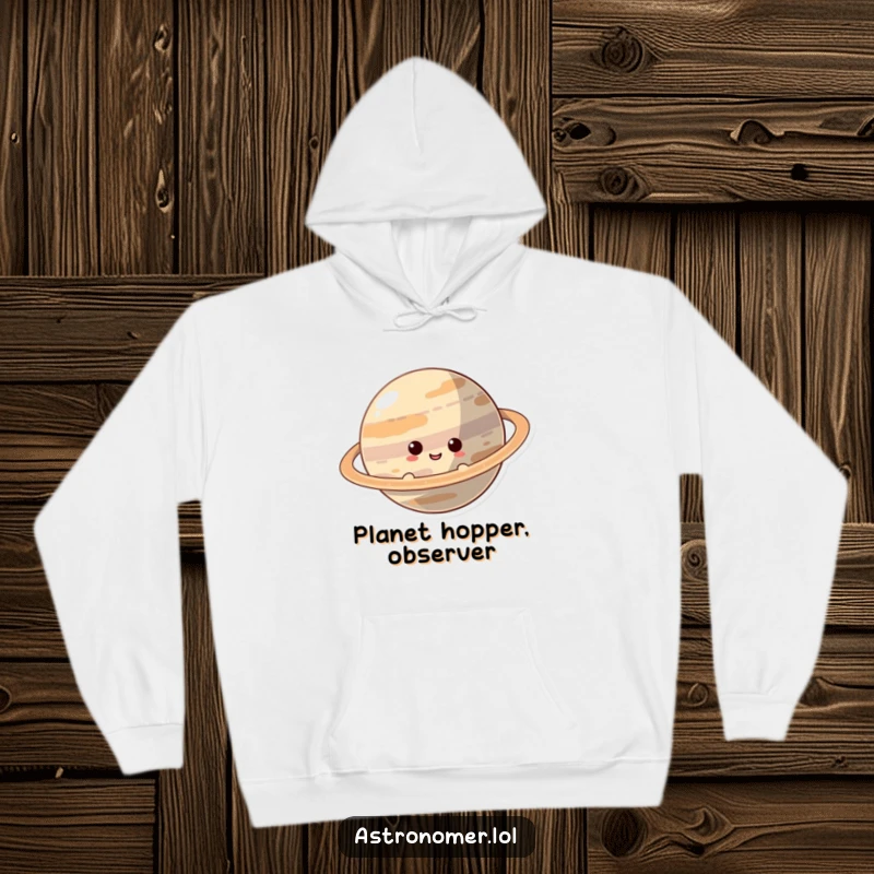 Funny Hoodie: A curious character smiles while peeking from behind a vast, ringed planet, inviting a sense of playful mystery.