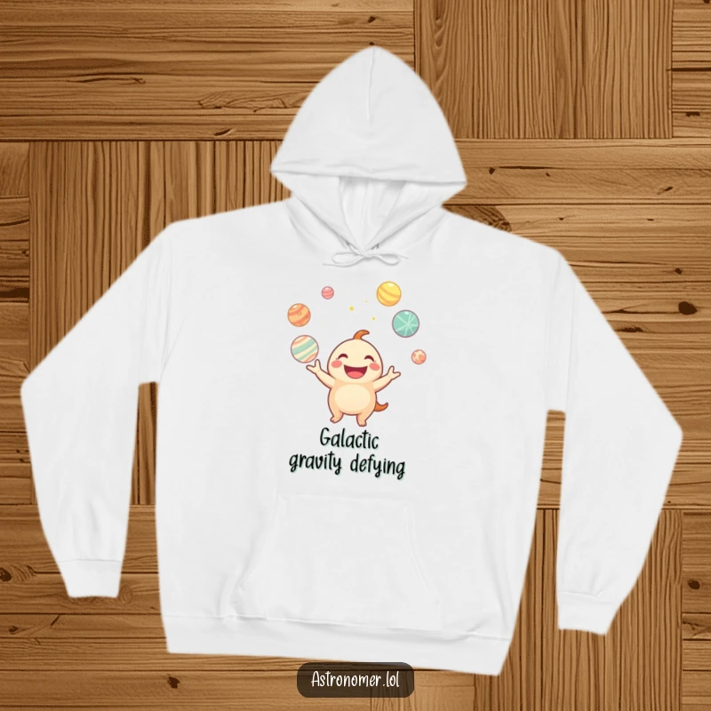 Funny hoodie with a graphic of a smiling creature juggling glowing planets, offering warmth and intergalactic humor.